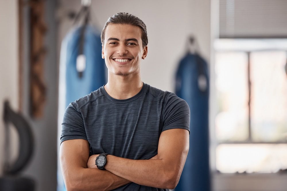 Propietario de un gym independiente con los brazos cruzados y sonriendo en el gimnasio